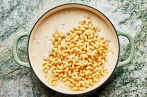 cooked macaroni being added to cheese sauce in a braiser