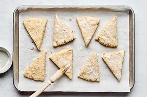 raw oat scones on a parchment lined baking sheet being brushed with yogurt