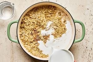 coconut milk being poured in a skillet with rice, green curry paste, soy sauce, fish sauce, sugar & water