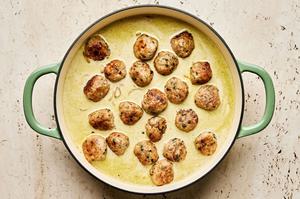 browned meatballs being added to a skillet with curry sauce and rice
