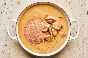 browned chicken thighs and red lentils added to a braiser with a coconut milk based broth