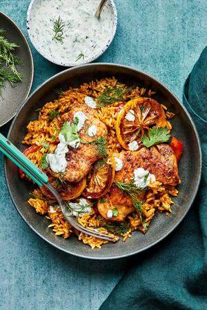 one pot chicken and rice in a bowl with a spoon topped with homemade herb yogurt next to a bowl of extra herb yogurt