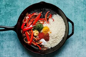 chicken stock, bell peppers, shallots, rice and spices being cooked in a skillet