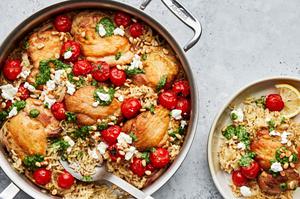 one pot pesto chicken and rice topped with goat cheese and pine nuts in a skillet being scooped on to a plate