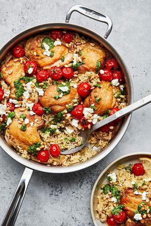 one pot pesto chicken and rice topped with goat cheese and pine nuts in a skillet being scooped on to a plate