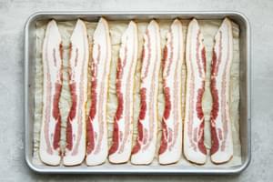 8 slices of raw bacon on a parchment paper lined baking sheet ready to be baked in the oven
