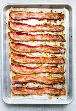 8 slices of baked bacon on a parchment lined baking sheet fresh out of the oven and perfectly crispy