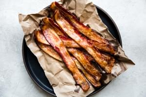 Oven baked bacon cooling on a parchment lined plate