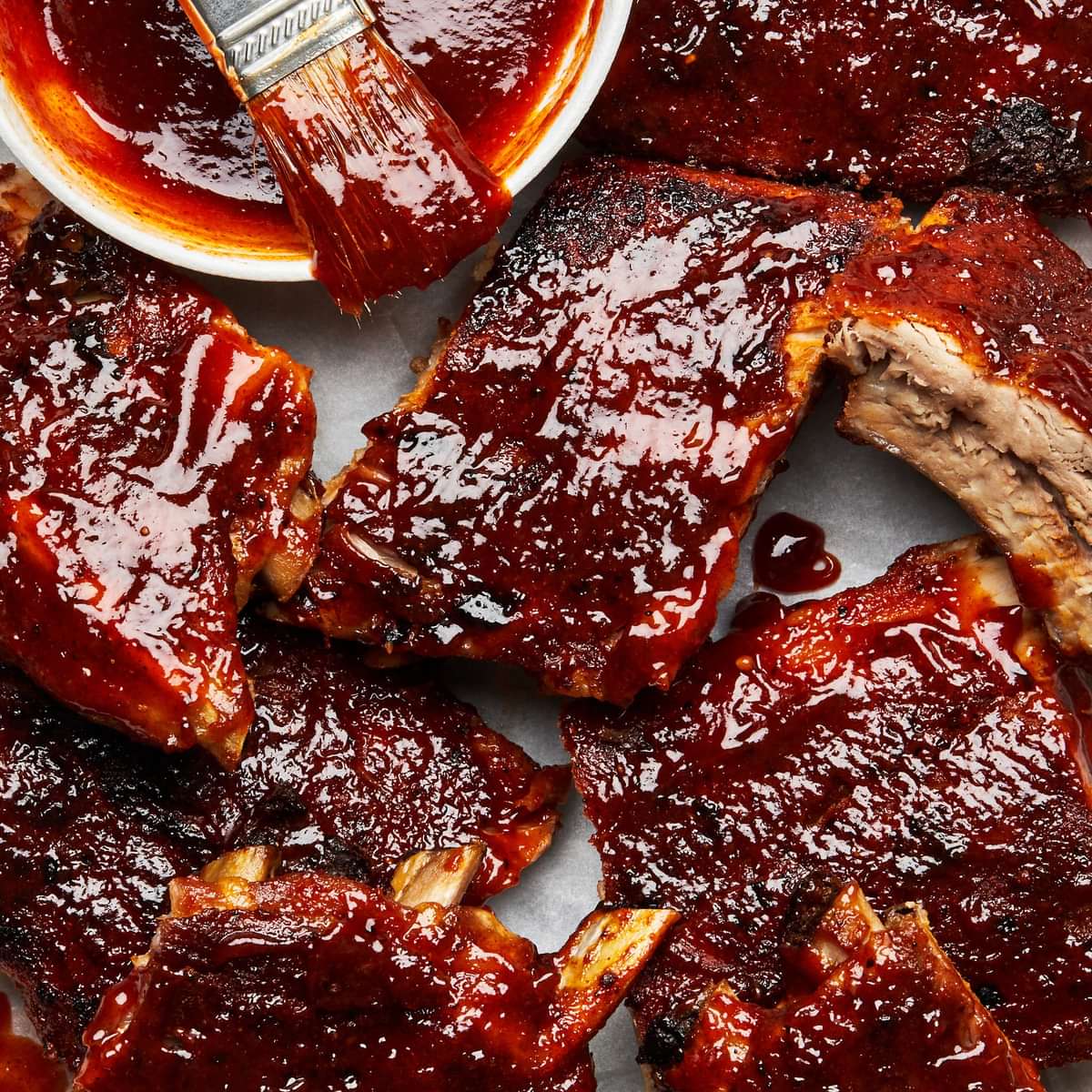 oven baked pork ribs being smothered in homemade bbq sauce