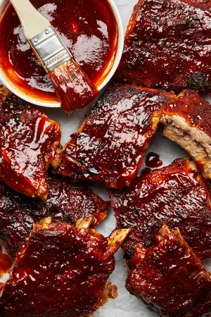 oven baked pork ribs being smothered in homemade bbq sauce