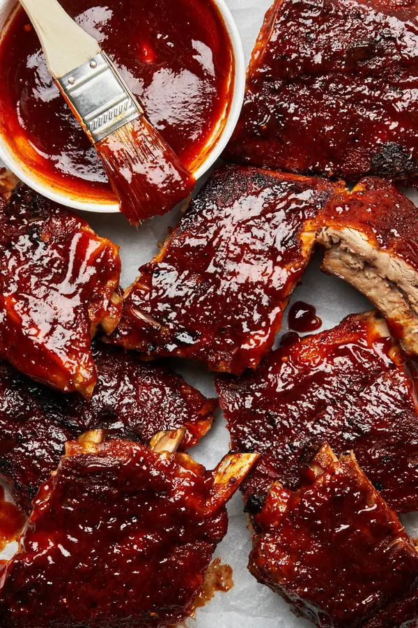 oven baked pork ribs being smothered in homemade bbq sauce