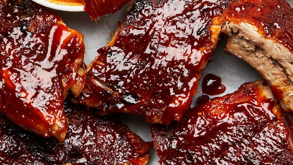oven baked pork ribs being smothered in homemade bbq sauce