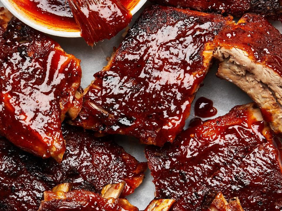 oven baked pork ribs being smothered in homemade bbq sauce