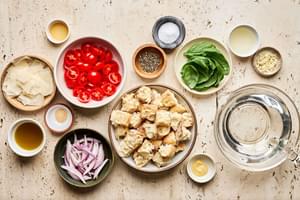 shallots, bread, olive oil, spices, basil, tomatoes and Parmesan in prep bowls to make Panzanella