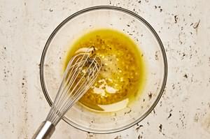 olive oil, honey, vinegar, garlic, mustard, salt, and pepper being whisked in a glass bowl