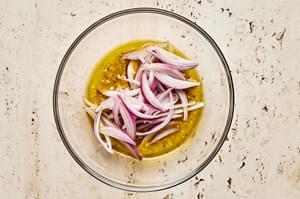 sliced shallots added to a bowl of homemade salad dressing