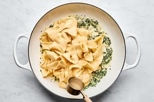 homemade pappardelle pasta being tossed with garlicky butter and fresh herb sauce in a skillet