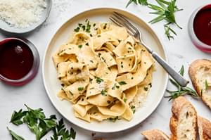 a plate of homemade pappardelle pasta topped with garlicky butter and fresh herb sauce served with crusty bread