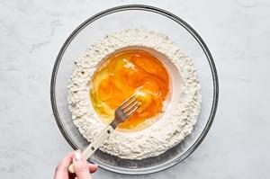 a large bowl with flour made into a well with eggs, olive oil and salt placed in the well