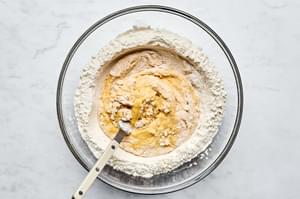 flour, olive oil, salt and eggs being combined with a fork in a large glass bowl