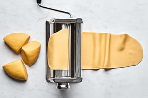 homemade pasta dough being rolled through a pasta maker