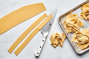 homemade pasta dough being sliced into long strips to make pappardelle