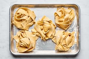 homemade pappardelle pasta noodles sprinkled with flour and curled in small nests