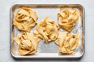 homemade pappardelle pasta noodles sprinkled with flour and curled in small nests