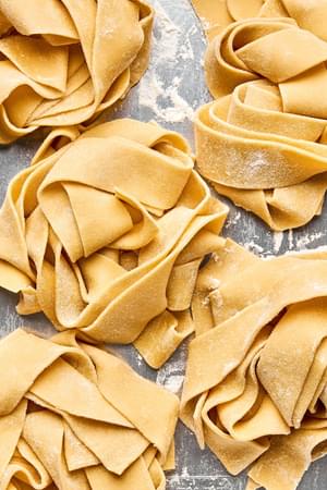 homemade pappardelle pasta noodles sprinkled with flour and curled in small nests