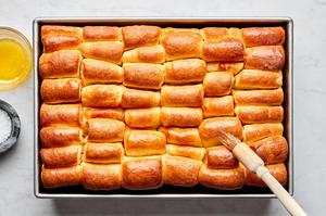 baked homemade parker house rolls on a baking sheet being brushed with melted butter and sprinkled with flaky salt