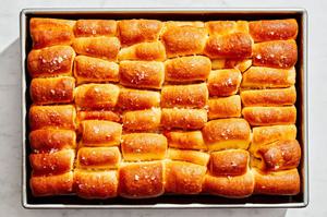 baked homemade parker house rolls on a baking sheet brushed with melted butter and sprinkled with flaky salt