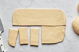 rolled parker house dough being sliced with a knife into small rectangles