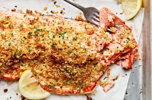 homemade parmesan crusted salmon on parchment paper being flaked with a fork, served with lemon wedges