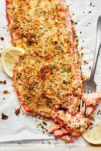 homemade parmesan crusted salmon on parchment paper flaked with a fork and served with lemon wedges