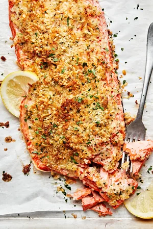 homemade parmesan crusted salmon on parchment paper flaked with a fork and served with lemon wedges