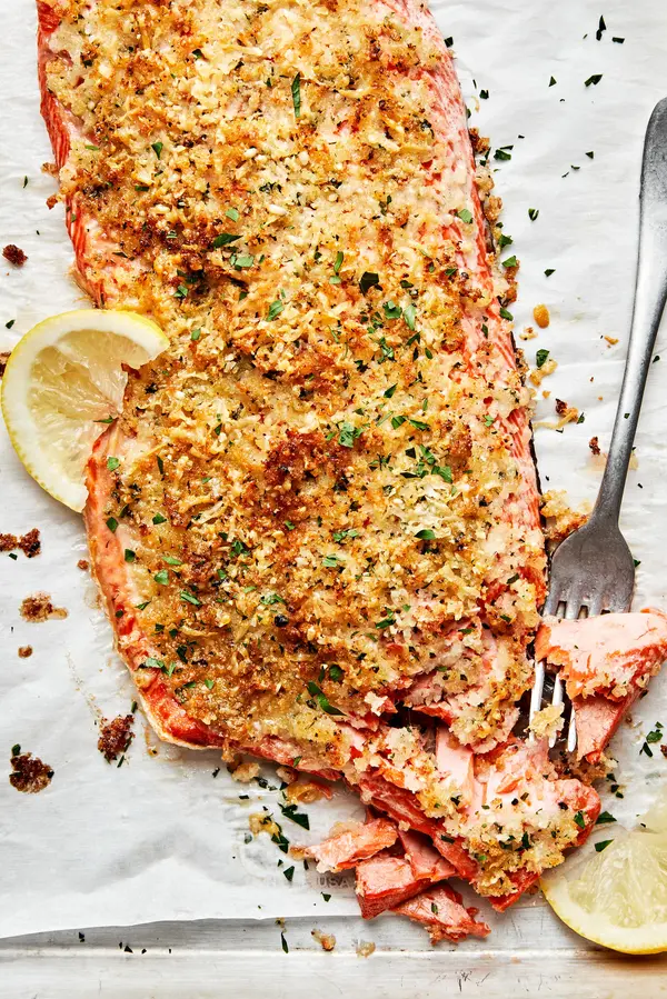 homemade parmesan crusted salmon on parchment paper flaked with a fork and served with lemon wedges