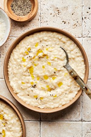 a bowl of homemade parmesan risotto drizzled with olive oil and topped with freshly cracked pepper with a spoon in it