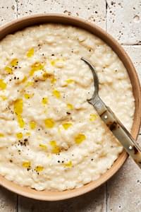 a bowl of homemade parmesan risotto drizzled with olive oil and topped with freshly cracked pepper with a spoon in it