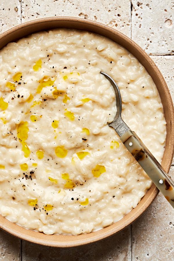 a bowl of homemade parmesan risotto drizzled with olive oil and topped with freshly cracked pepper with a spoon in it