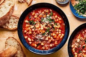 a bowl of homemade pasta e fagioli sprinkled with parsley and parmesan surrounded by slices of crusty bread