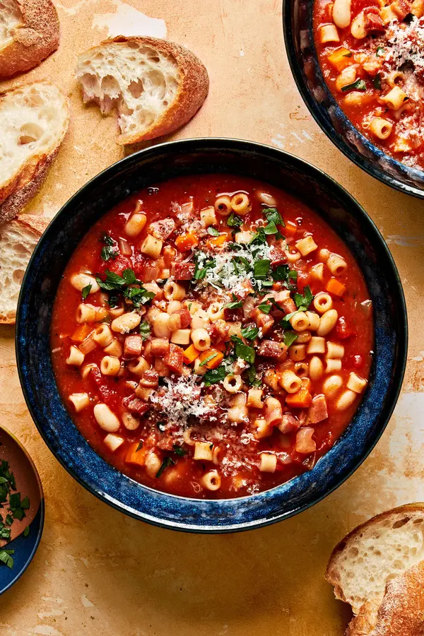 a bowl of homemade pasta e fagioli sprinkled with parsley and parmesan surrounded by slices of crusty bread