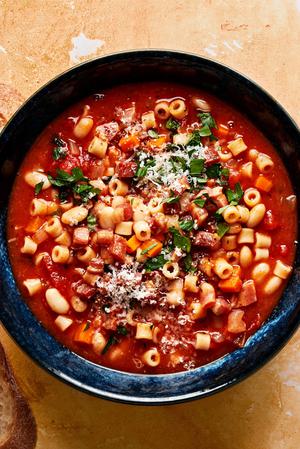 a bowl of homemade pasta e fagioli sprinkled with parsley and parmesan surrounded by slices of crusty bread