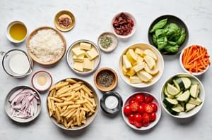 pasta, carrots, zucchini, squash, cherry tomatoes, sun dried tomatoes, butter, milk, Parmesan and spices in prep bowls
