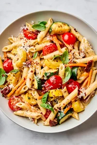 a bowl of past primavera made with zucchini, squash, carrots, sun dried tomatoes, cherry tomatoes and parmesan