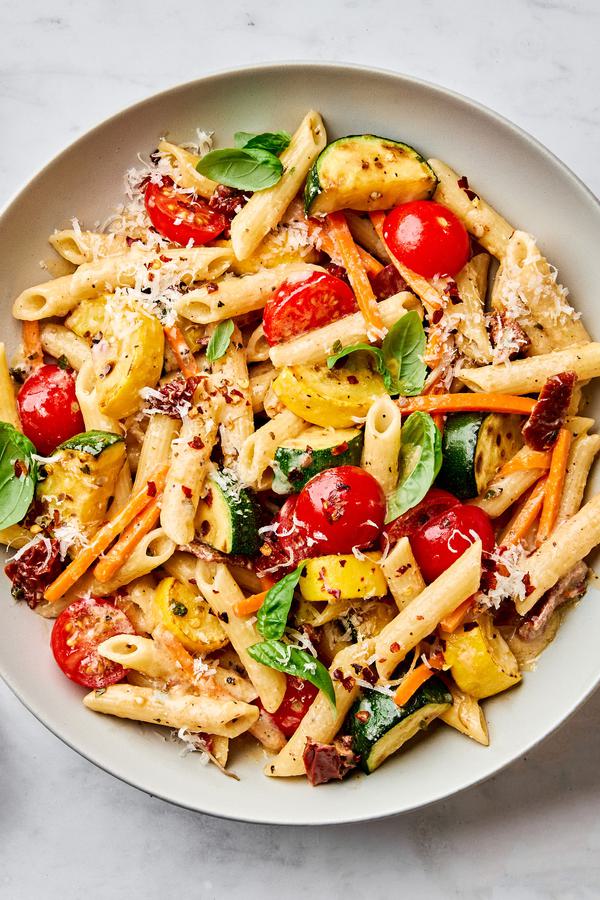 a bowl of past primavera made with zucchini, squash, carrots, sun dried tomatoes, cherry tomatoes and parmesan