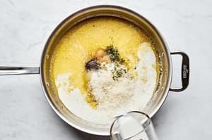 milk being poured into a skillet with butter Parmesan, dried basil, garlic powder, salt & pepper