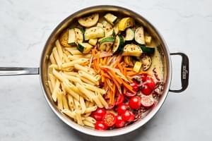pasta, zucchini, squash, sun dried tomatoes, cherry tomatoes and sauce being tossed in a skillet