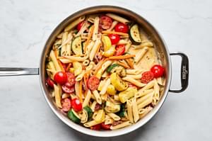 a pan of past primavera made with zucchini, squash, carrots, sun dried tomatoes, cherry tomatoes and parmesan