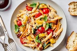 a bowl of past primavera made with zucchini, squash, carrots, sun dried tomatoes, cherry tomatoes and parmesan