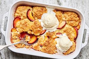 homemade peach cobbler in a baking dish topped with 2 scoops of vanilla ice cream